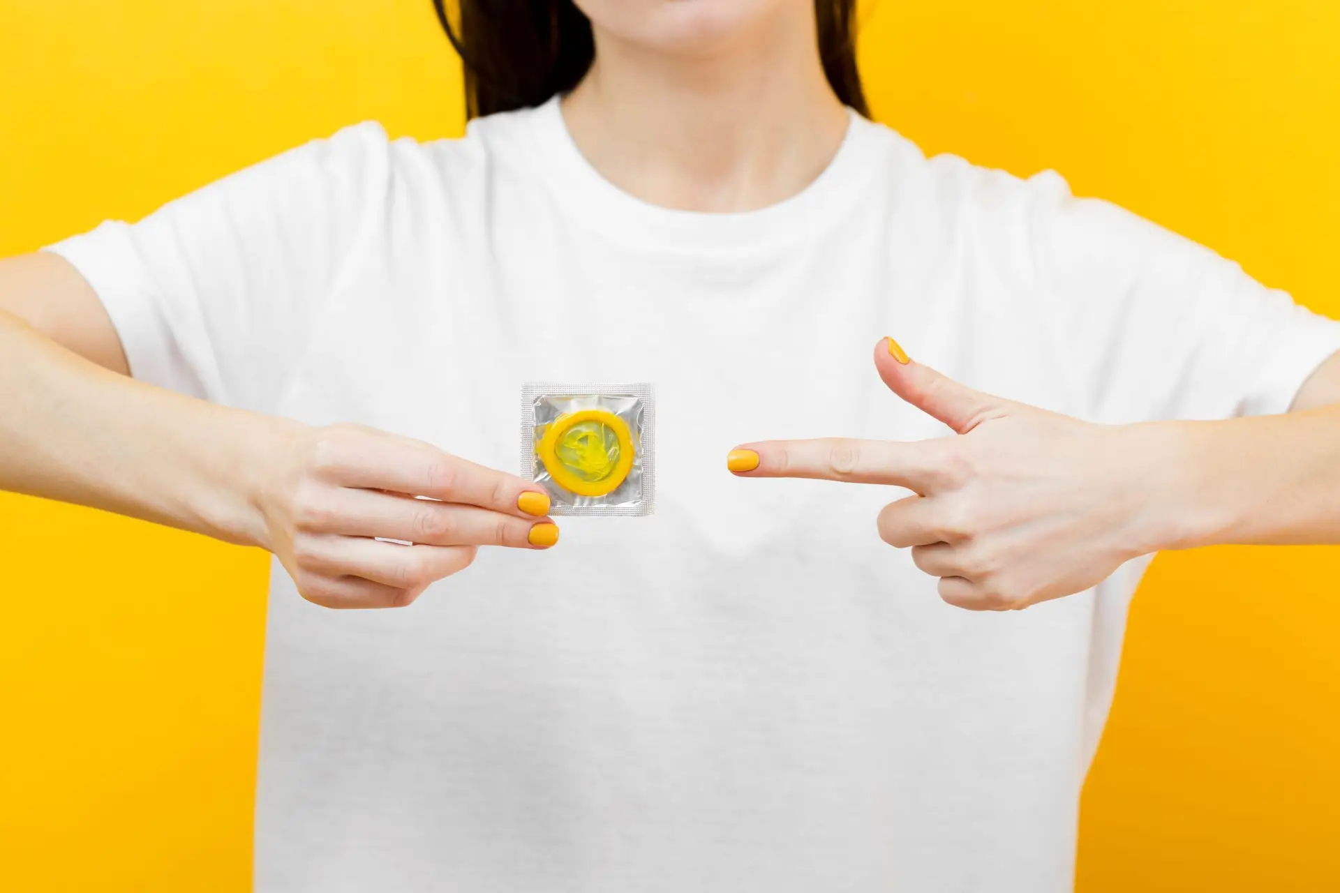 Person holding up a yellow condom between their fingers against a neutral background.