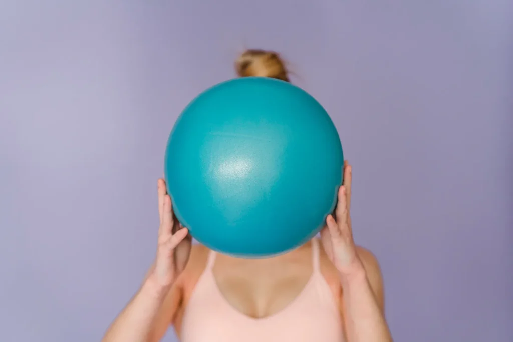 Woman holding a teal fitness ball in front of her face on a lilac background, a pelvic floor theme for a kegel balls guide