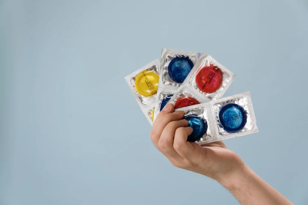 Hand holding a fan of colorful condom packets against a light blue background for a latex free condoms guide